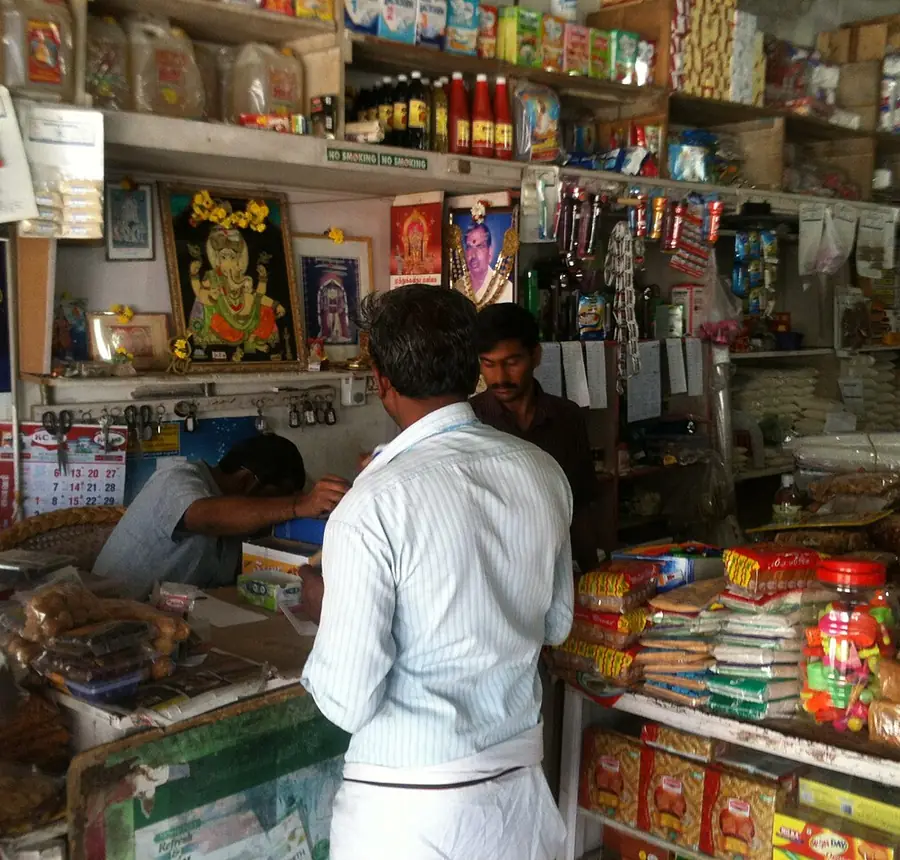 Shopkeeper behind the counter of a neighbourhood kirana store stocked floor to ceiling